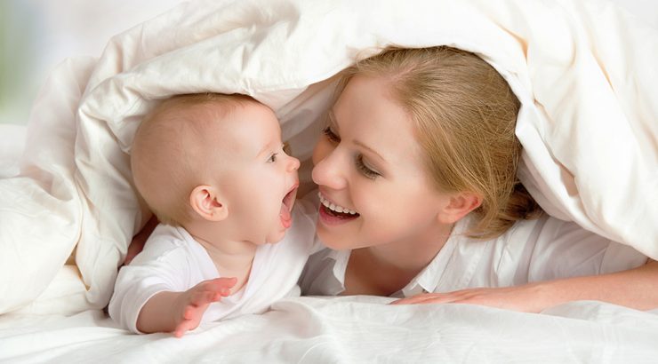 Mamma och baby leker under täcket