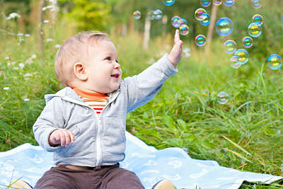 A baby boy sits in a green meadow playing with soap bubbles