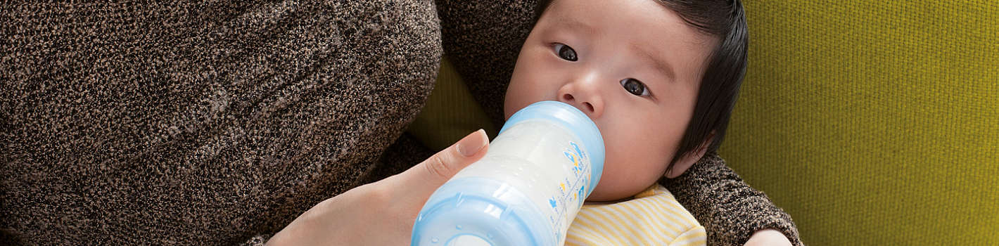 Mutter füttert Baby auf Couch mit blauer MAM Easy Start Anti-Colic Flasche