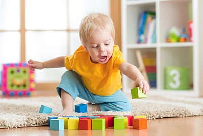Baby boy with blond hair plays with coloured wooden blocks in a playroom 