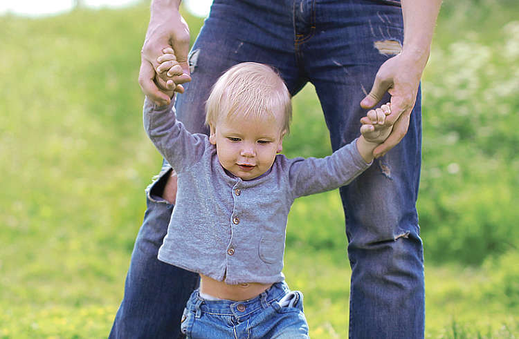 A baby boy walks across a meadow, holding his father's hands firmly A baby boy walks across a meadow, holding his father's hands firmly