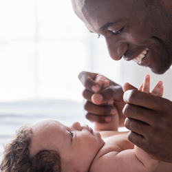 Happy father bends over his laughing baby and holds its hands Happy father bends over his laughing baby and holds its hands