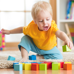 Young boy playing with wooden blocks on floor at home