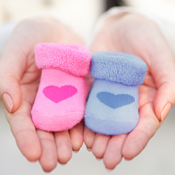 Someone holds one pink baby sock and one blue baby sock in their hands