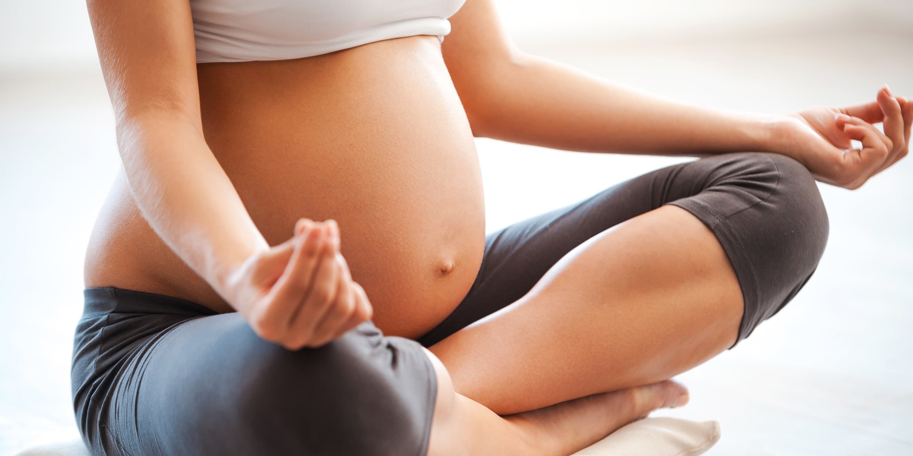 Schwangere Frau sitz in Yoga-Position auf dem Boden