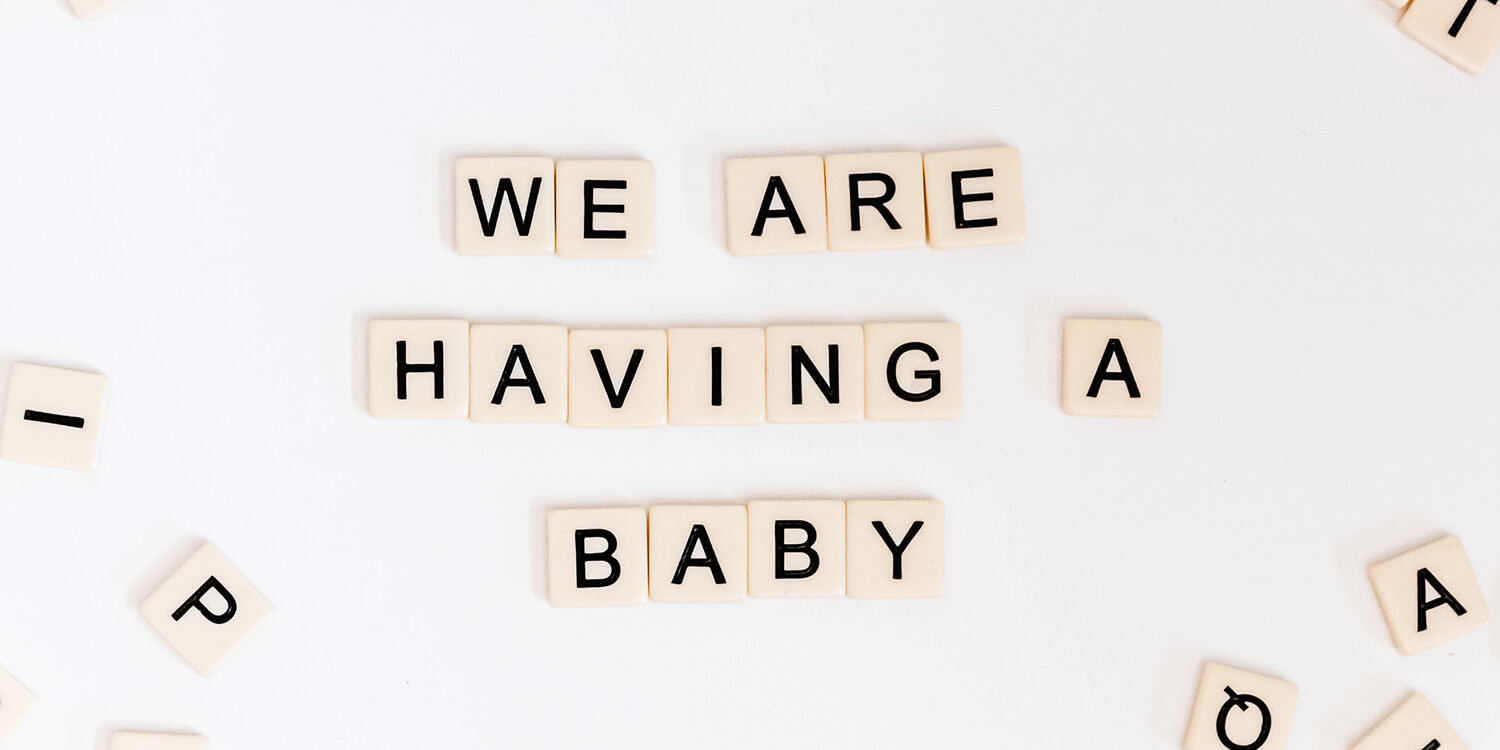 Buchstabensteine bilden den Text „Wir bekommen ein Baby“ (12. SSW) 