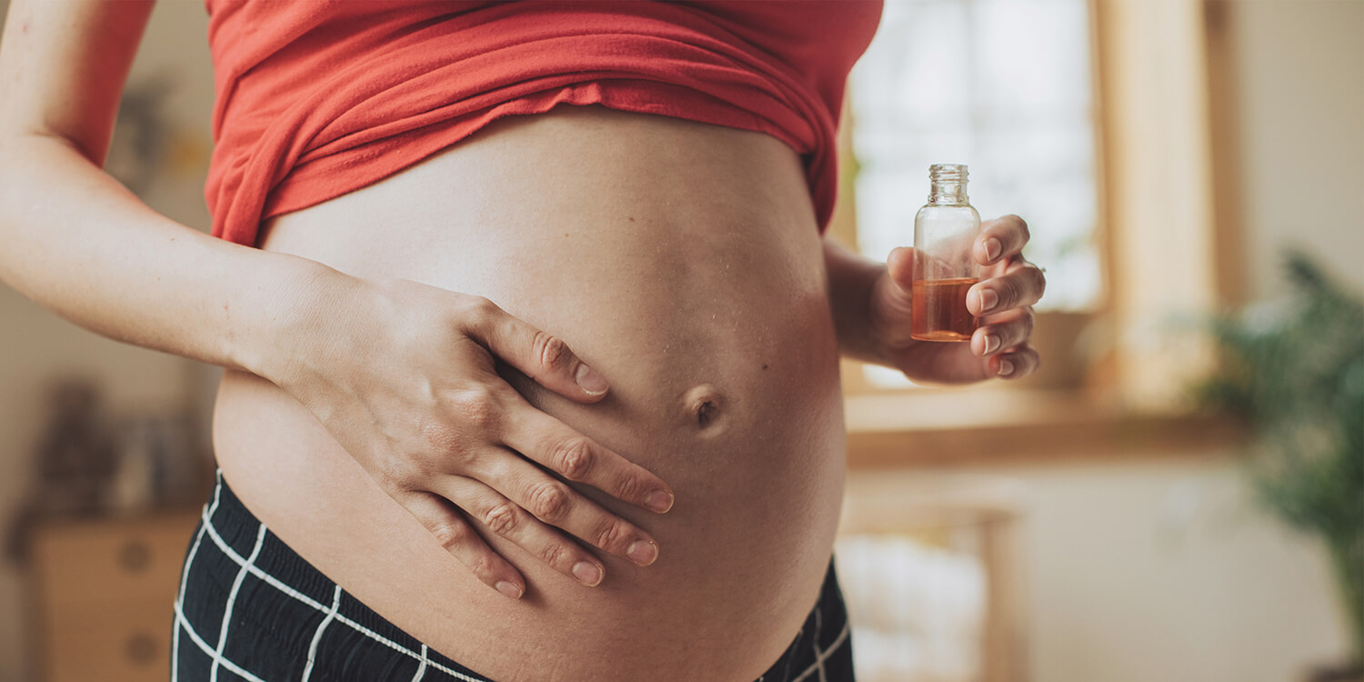 Schwangere Frau reibt Öl auf ihren Bauch. 
