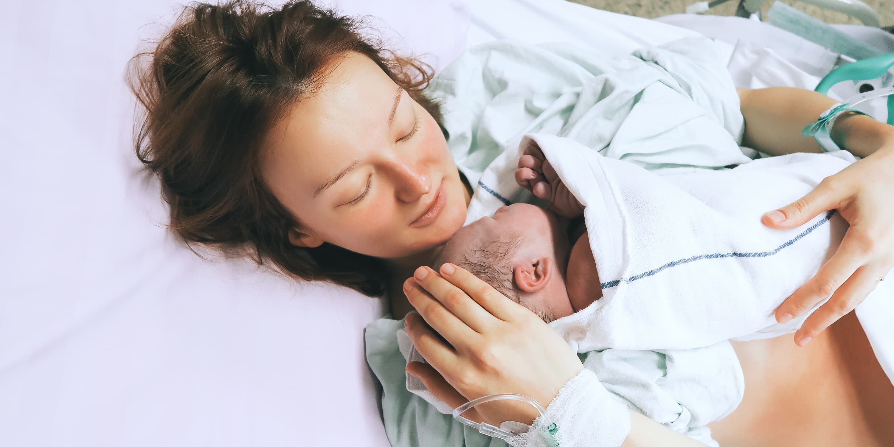 Frau liegt im Krankenhausbett und hält ihr Neugeborenes im Arm
