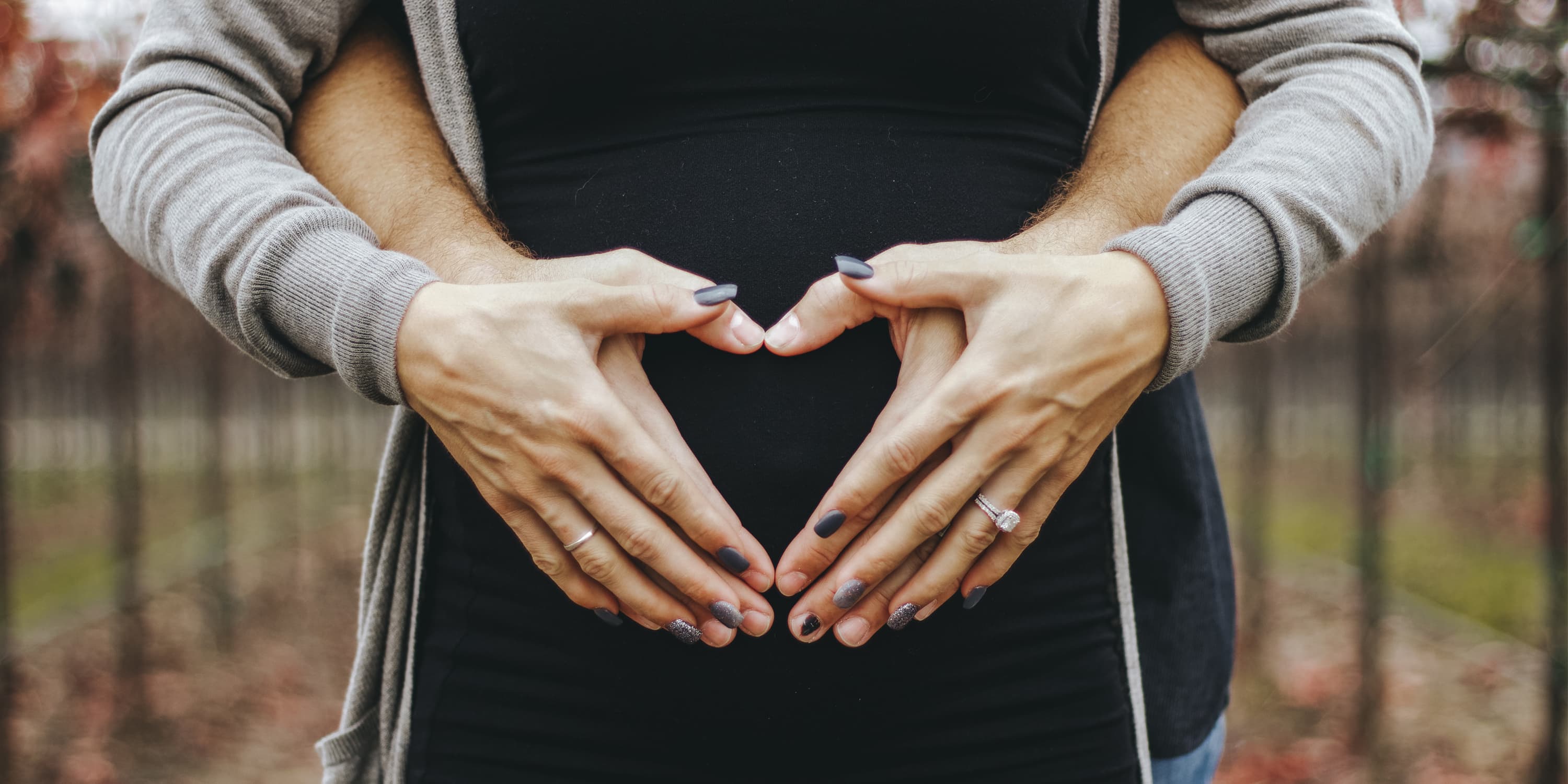 Mann und Frau formen Herz mit ihren Händen auf dem Babybauch der Frau