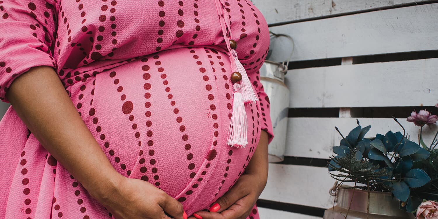 Een detailfoto van een zwangere vrouw die haar handen onder haar babybuik houdt.